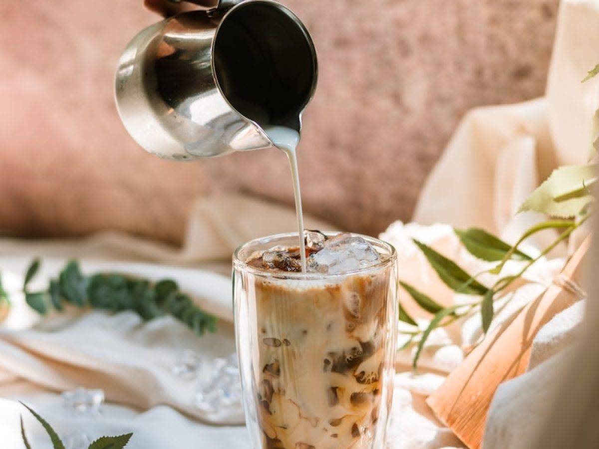 person pouring brown liquid on white and brown ceramic mug