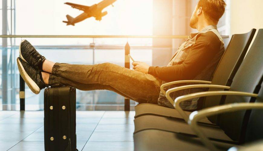 man sitting on gang chair with feet on luggage looking at airplane