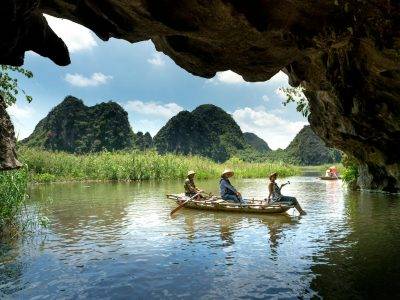 Explore a scenic river cave with lush mountain views in a traditional boat adventure.