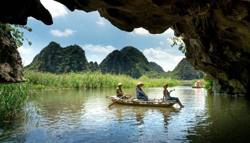 Explore a scenic river cave with lush mountain views in a traditional boat adventure.