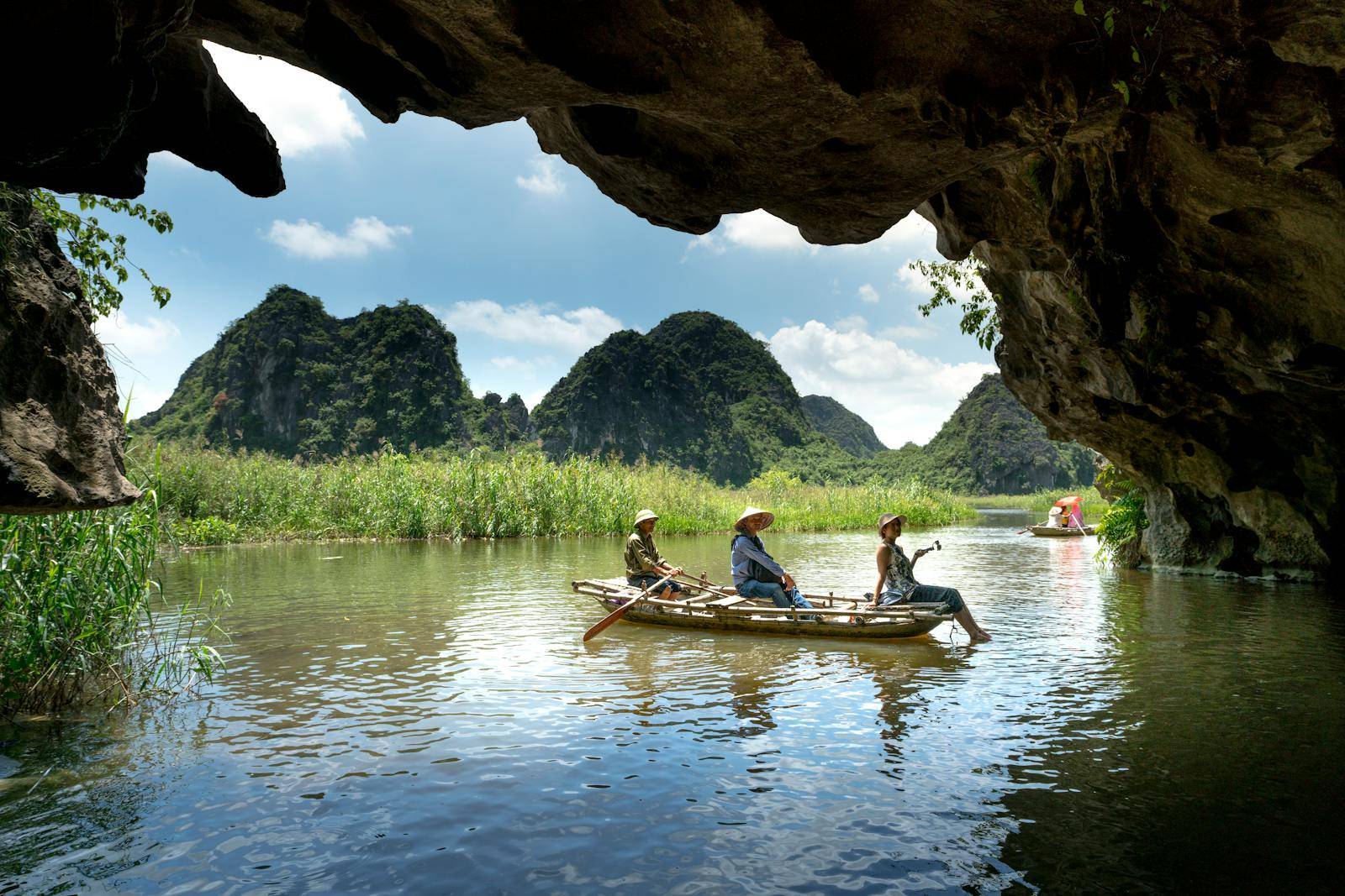 Explore a scenic river cave with lush mountain views in a traditional boat adventure.