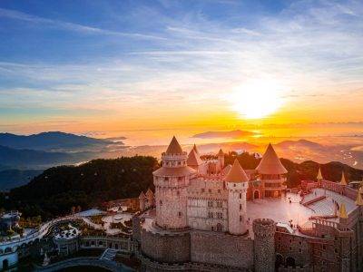 A breathtaking aerial view of a majestic castle with a vibrant sunset backdrop over the mountains.