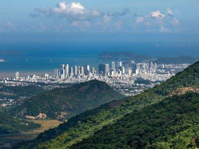 A breathtaking view of a city skyline by the sea from a mountainous landscape.