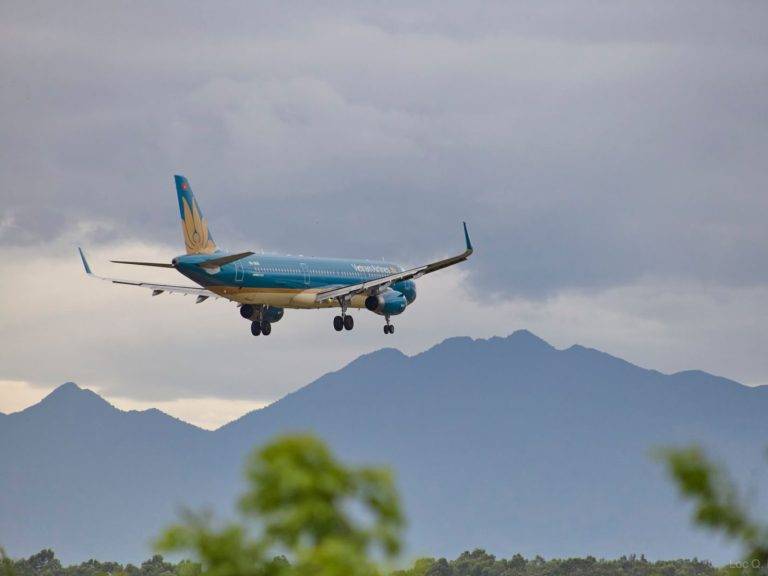Airplane approaching Đà Nẵng Airport with scenic mountains in the backdrop.