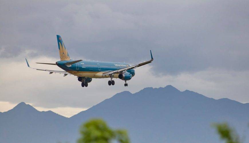 Airplane approaching Đà Nẵng Airport with scenic mountains in the backdrop.
