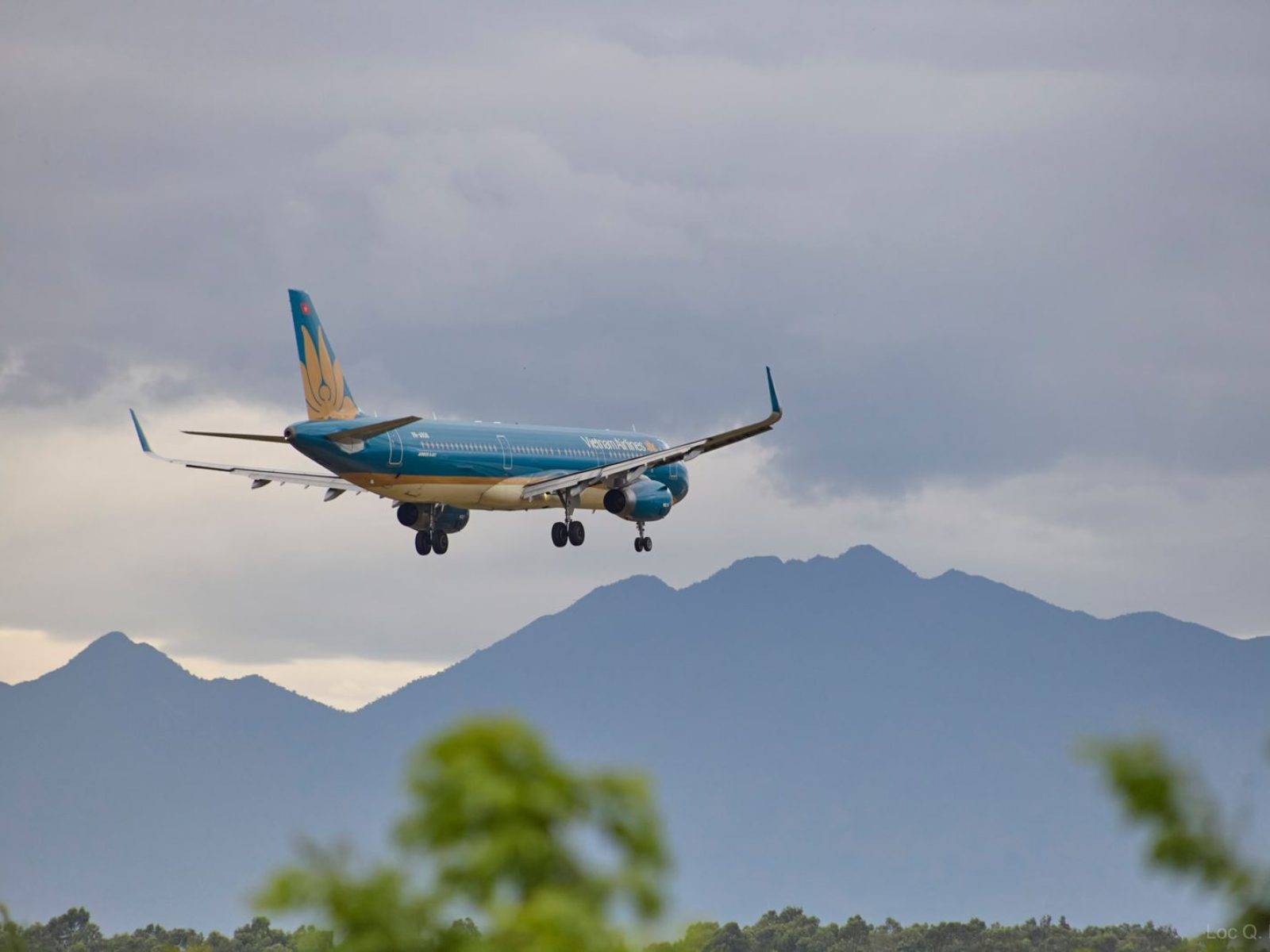 Airplane approaching Đà Nẵng Airport with scenic mountains in the backdrop.